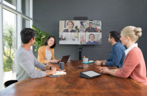 two women and two men sitting at a table in front of a screen attending a hybrid meeting